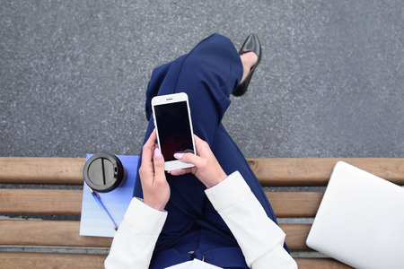 Young woman with mobile phone resting on bench outdoorsの写真素材