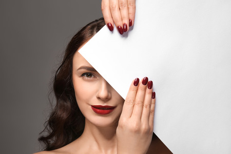 Beautiful young woman with professional manicure and blank poster on grey backgroundの写真素材