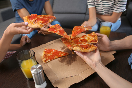 Young people taking slices of delicious pizza from cardboard box on tableの写真素材