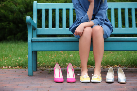 Young woman with different pairs of shoes sitting on bench outdoorsの写真素材