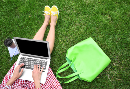 Young woman with laptop resting on green grass in parkの写真素材