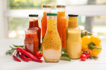 Glassware with different tasty sauces and vegetables on white tableの写真素材