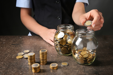 Woman putting coins into glass jar on table. Savings conceptの写真素材
