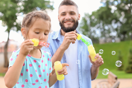 Little girl and her father blowing soap bubbles outdoorsの写真素材
