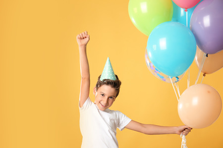 Cute little boy in Birthday hat and with balloons on color backgroundの写真素材