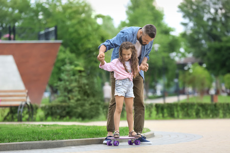 Father teaching his little daughter to ride skateboard outdoorsの写真素材