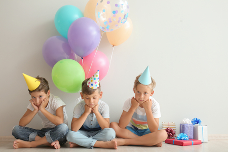 Cute little children in Birthday hats sitting on floor near light wallの写真素材