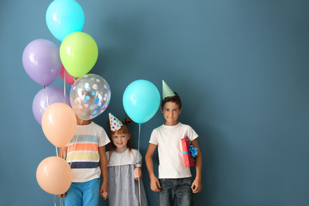 Cute little children in Birthday hats and with balloons on color backgroundの写真素材
