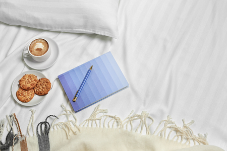 Cup of coffee, cookies and notebook on bed linenの写真素材