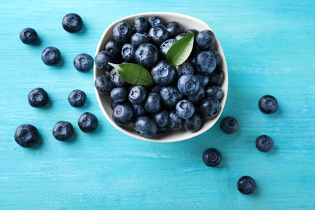 Bowl with ripe blueberries on color tableの写真素材