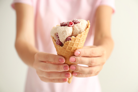 Woman holding waffle cone with delicious ice cream and raspberries on light background, closeupの写真素材