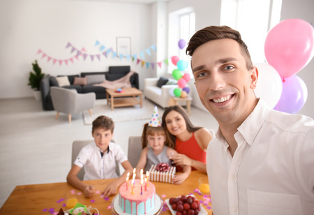 Young man taking selfie with family while celebrating daughter's birthday at homeの写真素材