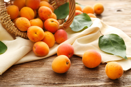 Wicker basket with ripe sweet apricots on wooden tableの写真素材