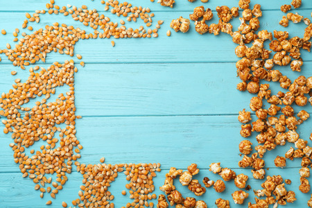 Frame made of delicious popcorn and kernels on wooden background