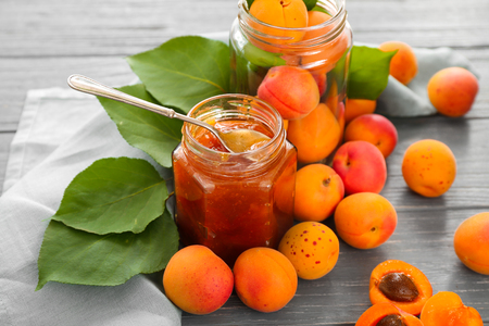 Glass jar with sweet apricot jam and fresh fruit on wooden tableの写真素材