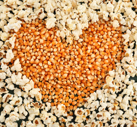 Heart made of delicious popcorn and kernels on table