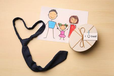 Child's drawing of family, gift box and necktie on wooden background. Father's Day celebrationの写真素材