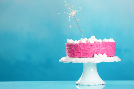 Stand with delicious birthday cake and sparkler on table against color backgroundの写真素材