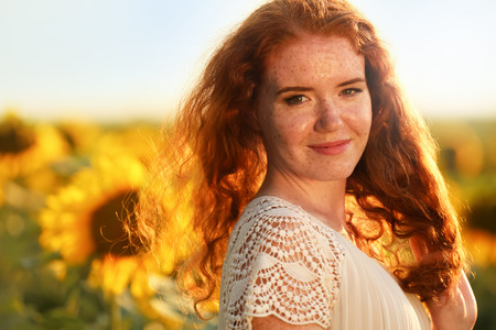 Beautiful redhead woman in sunflower field on sunny dayの写真素材