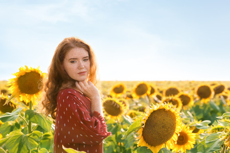 Beautiful redhead woman in sunflower field on sunny dayの写真素材