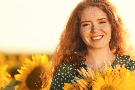 Beautiful redhead woman in sunflower field on sunny dayの写真素材