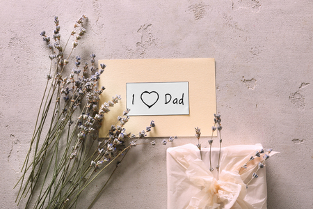 Handmade card with phrase "I LOVE DAD", gift box and lavender flowers on textured background. Father's day celebrationの写真素材