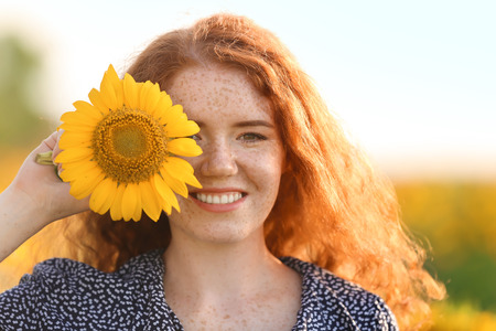Beautiful redhead woman in sunflower field on sunny dayの写真素材