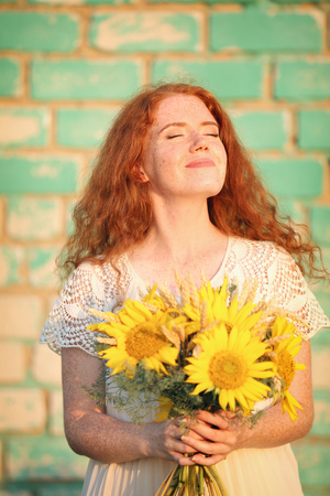Beautiful redhead woman with sunflowers against brick wallの写真素材