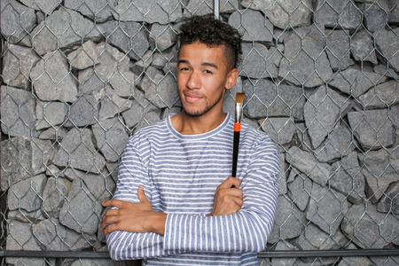 Young African-American artist with brush against stone wall