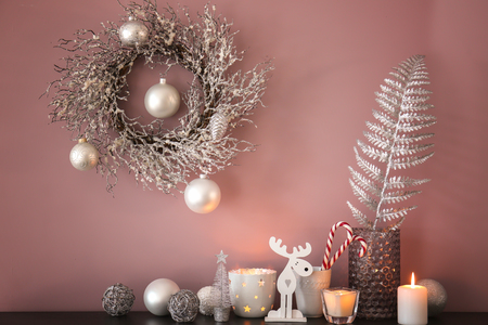Burning candles and Christmas decorations on table with wreath hanging on color wallの写真素材