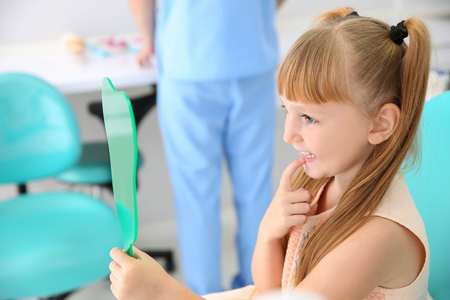 Cute little girl looking in mirror at dentist's officeの写真素材