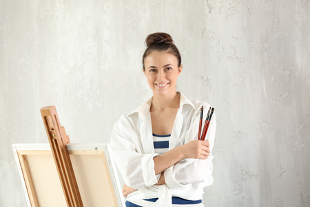 Female artist with brushes and easel on grey backgroundの写真素材