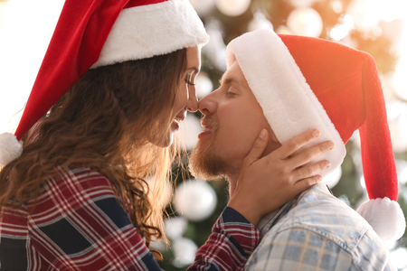 Cute young couple in Santa hats celebrating Christmas at homeの写真素材
