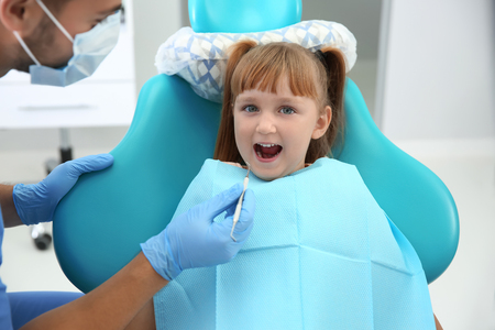 Dentist examining little girl's teeth in clinicの写真素材