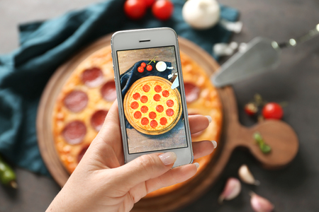 Woman taking photo of tasty Pepperoni pizza on tableの写真素材