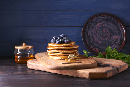 Board with tasty pancakes, honey dipper and blueberries on wooden tableの写真素材