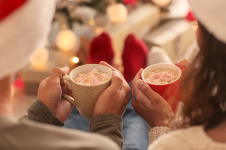 Cute young couple drinking hot chocolate on Christmas eve at homeの写真素材