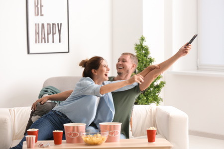 Couple fighting for remote control while watching TV at homeの写真素材