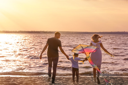 Happy family flying kite near river at sunsetの写真素材