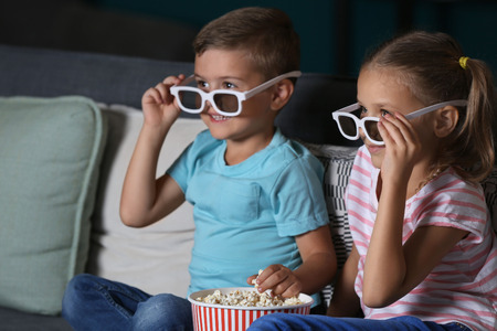 Children eating popcorn while watching TV in eveningの写真素材