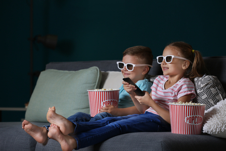 Children eating popcorn while watching TV in eveningの写真素材