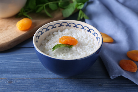 Bowl with delicious rice pudding and dried apricot on wooden tableの写真素材