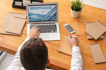 Man taking notes while using laptop to pay mortgage loan online in officeの写真素材