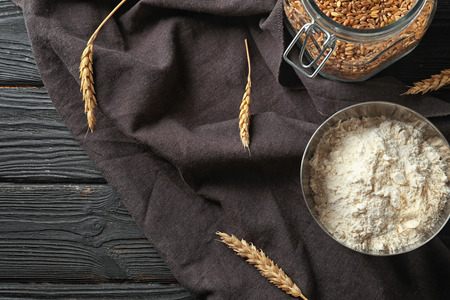 Bowl with wheat flour and jar of grains on wooden backgroundの写真素材