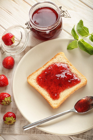 Plate with slice of bread and delicious strawberry jam on white wooden tableの写真素材