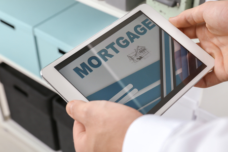 Man using tablet computer to pay mortgage loan online in office, closeupの写真素材