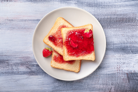 Plate with slices of bread and delicious strawberry jam on wooden tableの写真素材
