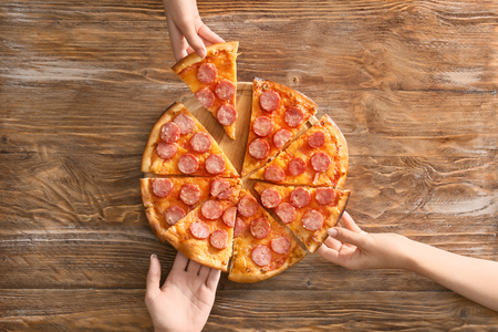 Young people taking slices of tasty pizza from wooden tableの写真素材