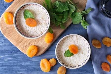 Bowls with delicious rice pudding and dried apricot on wooden tableの写真素材