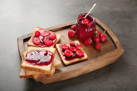 Board with slices of bread and delicious strawberry jam on dark tableの写真素材
